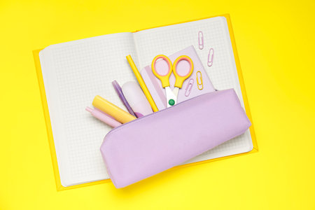 Pencil case and different stationery on yellow background, top view