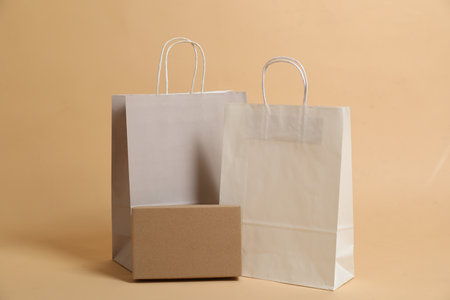 Blank shopping bags and cardboard box for branding on beige background. Mockup for design