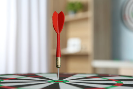 Red arrow hitting target on dart board indoors, closeup