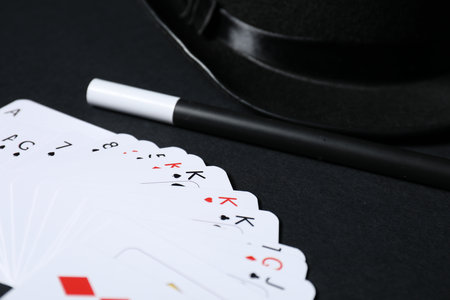 Playing cards, hat and magic wand on black background, closeup