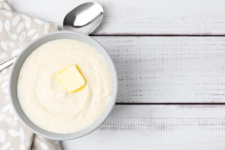 Tasty cooked semolina porridge with butter and spoon on white wooden table, top view. Space for textの写真素材