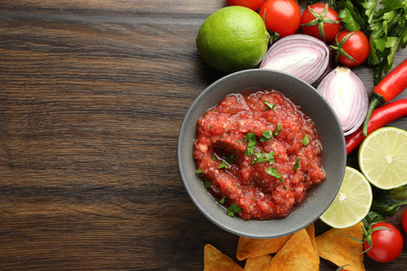 Delicious spicy salsa sauce in bowl and products on wooden table, flat lay. Space for textの写真素材