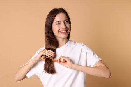 Smiling woman brushing her hair with comb on beige backgroundの写真素材