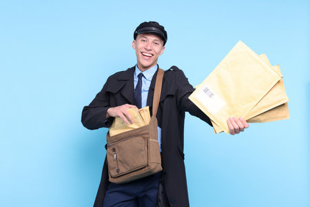 Happy postman with bag giving envelopes on light blue background