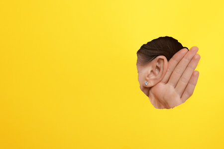 Woman showing hand to ear gesture through hole in yellow paper, closeup.の写真素材