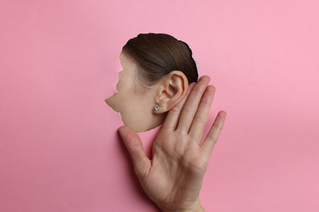 Woman showing hand to ear gesture through hole in pink paper, closeupの写真素材