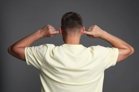Man covering his ears with fingers on gray background, back viewの写真素材