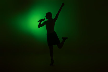 Silhouette of woman singing on dark background with green lightの写真素材