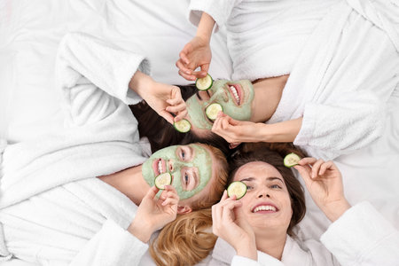 Spa day. Beautiful woman with face masks and cucumber slices on bed, above viewの写真素材