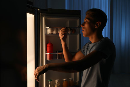 Young man suffering from sleepwalking near fridge at homeの写真素材