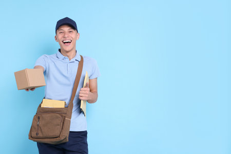 Happy postman with bag, envelopes and parcel on light blue background. Space for textの写真素材