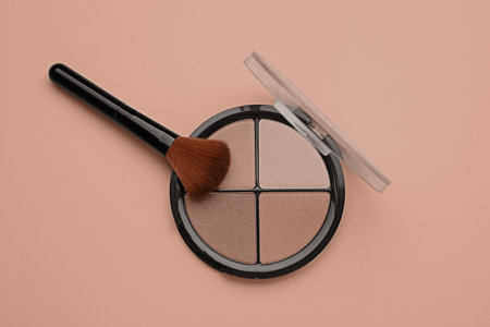 Eyeshadow palette in mocha mousse shades and makeup brush on dark beige background, top view. Trendy...