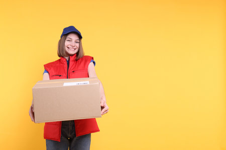 Happy postwoman giving parcel on yellow background. Space for textの写真素材