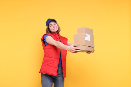 Happy postwoman with parcels on yellow background