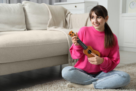 Happy woman playing ukulele on floor at homeの写真素材