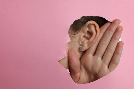 Woman showing hand to ear gesture through hole in pink paper, closeup. Space for textの写真素材
