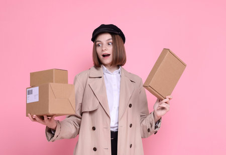 Surprised postwoman with parcels on pink background