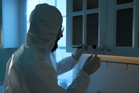 Forensic expert taking fingerprints from cupboard with brush at crime scene indoorsの写真素材