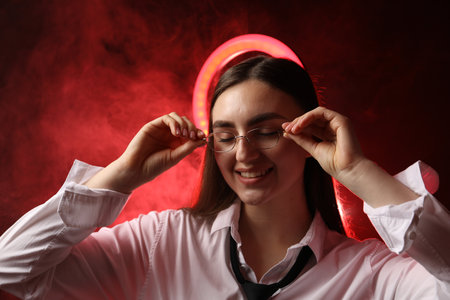 Beautiful woman with ring lamp wearing glasses on dark red background in smokeの写真素材