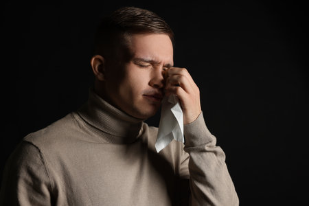 Crying man wiping tears with tissue on black backgroundの写真素材