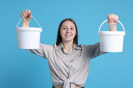 Woman with buckets of paint on light blue backgroundの写真素材