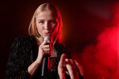 Beautiful singer performing on dark background with red light and smoke.