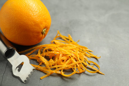 Orange zest, zester tool and fresh fruit on gray textured table, closeup. Space for text
