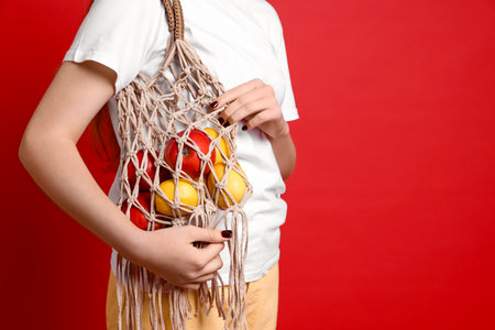 Teenage girl with handmade macrame bag on red background, closeup. Space for textの写真素材
