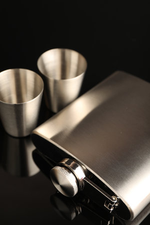 Hip flask and cups on black mirror surface, closeupの写真素材
