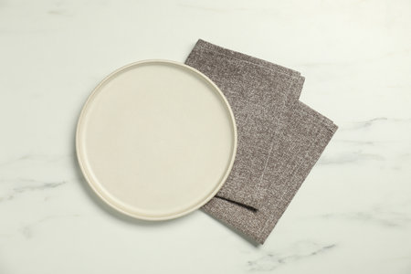 Gray napkin and empty plate on white marble table, top view