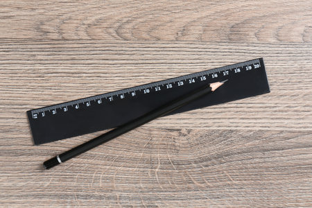 Black ruler and pencil on wooden table, top viewの写真素材