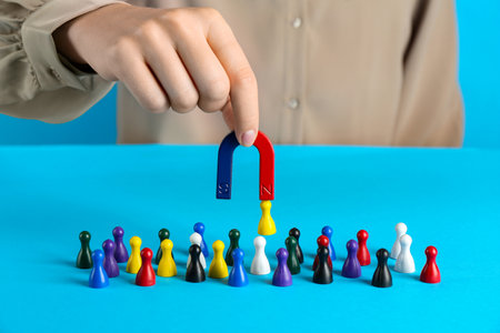 Woman with magnet attracting yellow piece among colorful ones on light blue background, closeupの写真素材