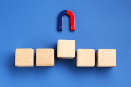 Magnet attracting wooden cubes on blue background, flat layの写真素材