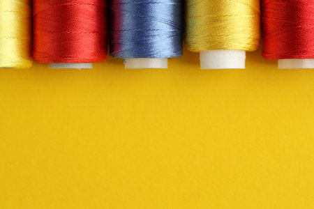 Different spools of sewing threads on yellow background, flat lay. Space for textの写真素材
