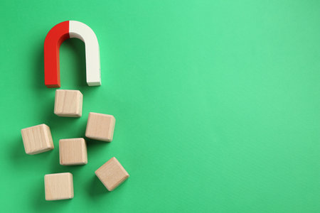 Magnet attracting wooden cubes on green background, flat lay. Space for textの写真素材