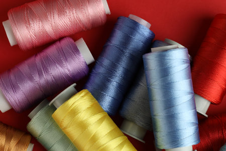Different spools of sewing threads on red background, top view