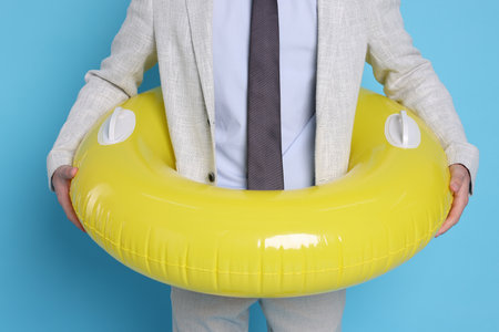 Businessman with inflatable ring on light blue background, closeupの写真素材