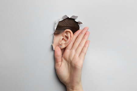 Woman showing hand to ear gesture through hole in grey paper, closeupの写真素材