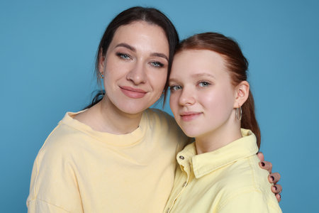 Portrait of beautiful mother with teenage daughter on light blue background