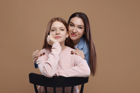 Portrait of beautiful mother with teenage daughter on dark beige backgroundの写真素材
