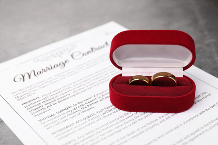 Marriage contract and golden rings on grey table, closeup