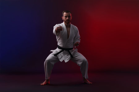 Man wearing uniform practicing karate in color lights against black backgroundの写真素材