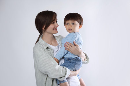 Beautiful mother with her cute little son on light grey backgroundの写真素材