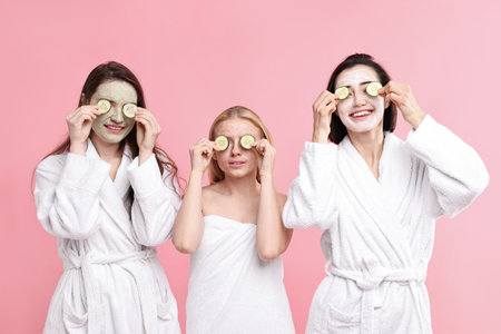Spa day. Happy women with face masks and cucumber slices on pink backgroundの写真素材