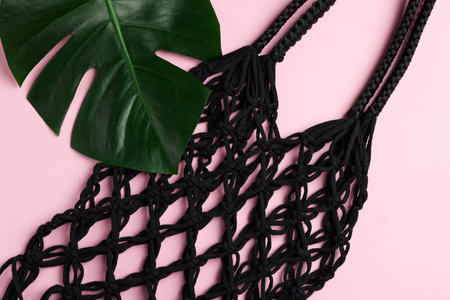 Macrame shopping bag and monstera leaf on pink background, top view
