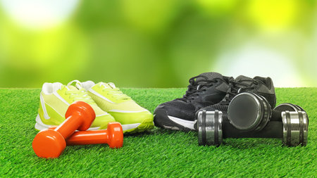 Sneakers and dumbbells on green grass, banner design. Sports equipmentの写真素材