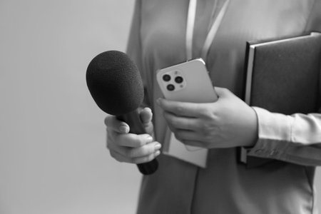 Journalist with microphone, mobile phone and notebook taking interview, closeup. Toned in...