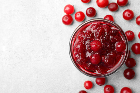 Tasty cranberry sauce in glass bowl and berries on light table, top view. Space for textの写真素材