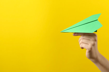 Woman with green paper plane on yellow background, closeup. Space for textの写真素材