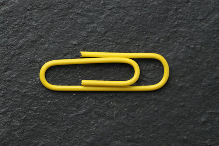 One yellow paper clip on black table, top view